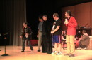 Cast members rehearse on stage inside a theater.   