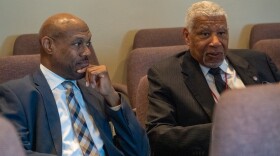  two men seated next to each other in suits