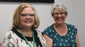 Two women sit next to each other smiling at the camera