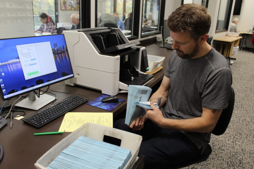 A worker at the Linn County Clerk’s Office sifts through ballots to make sure none stick together before he runs them through a counting machine and scanner that will capture the signature on each envelope.