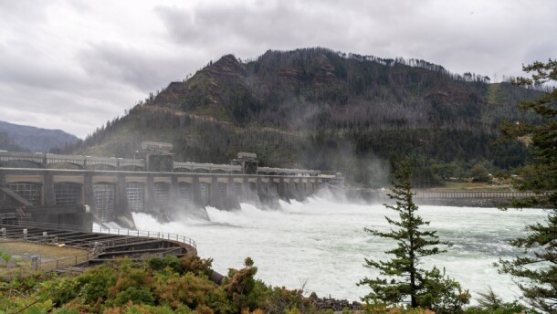 Water rushing through a dam in front of a hill. 