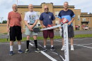Men stand on both sides of a pickleball net in front of an old school building.