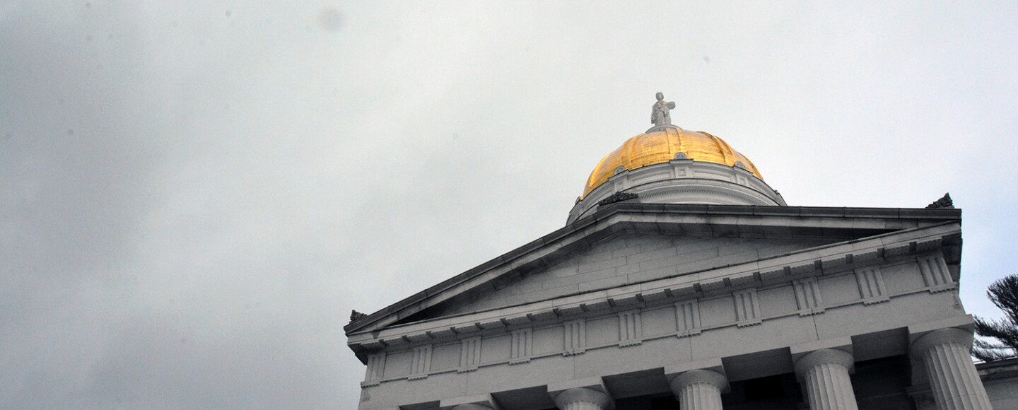 Looking up at the golden dome of the Vermont Statehouse on a cloudy day.