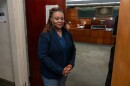 A woman in a blue blazer stands in front of an office door 