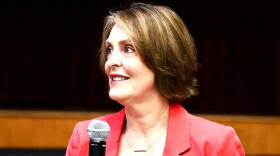 woman with short hair in peach-orange blazer holding microphone 