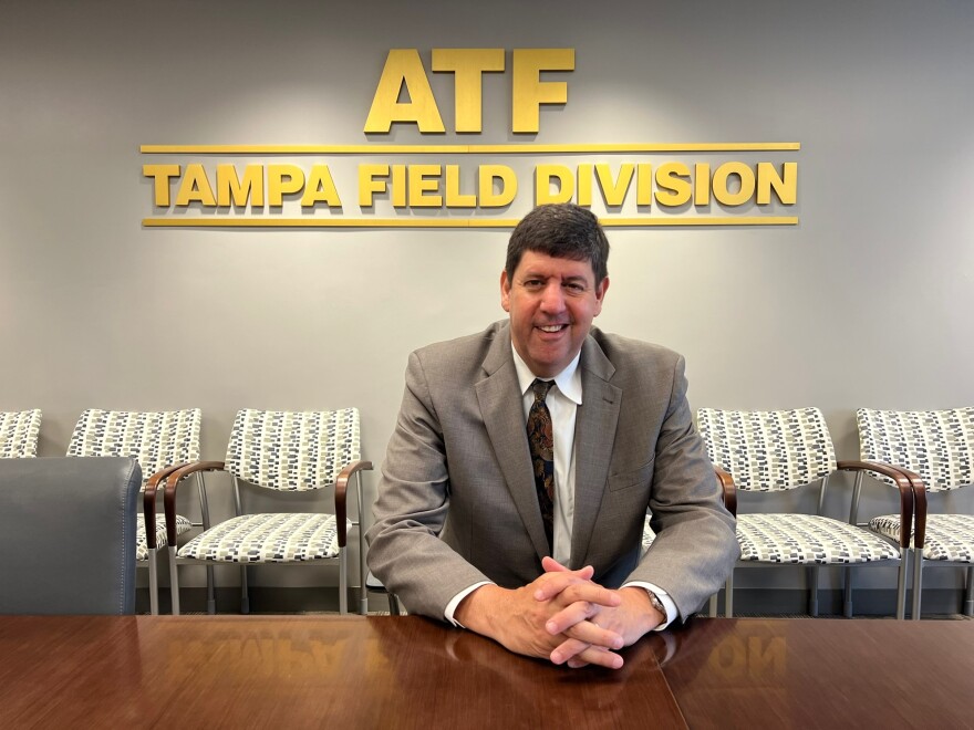 ATF director Steven Dettelbach sits in a conference room. A sign reading "ATF Tampa Field Division" is in the background.