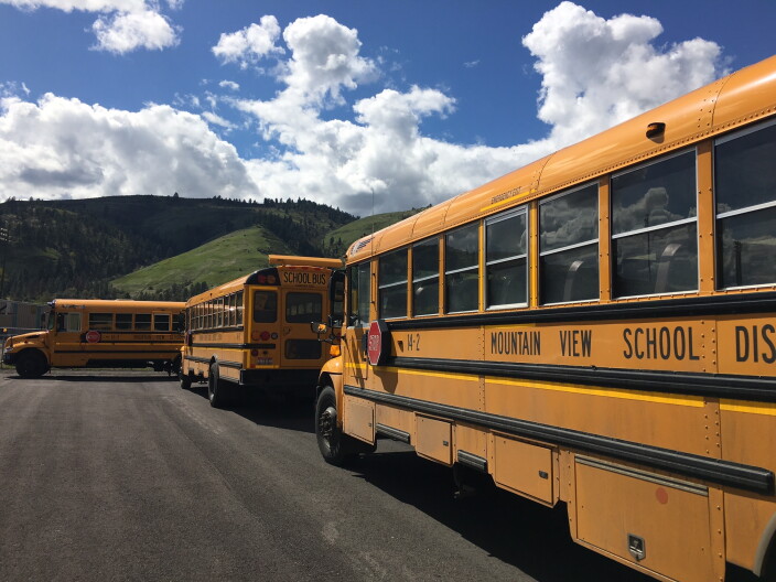 Three yellow school busses at different angles with mountains in the background.