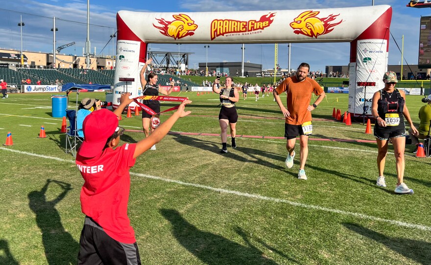 A young volunteer holds up a finisher's medal for Nathan Cox of Bel Aire. Dozens of volunteers waited with medals, water and support for runners who made it to the finish line at the field at Equity Bank Park.