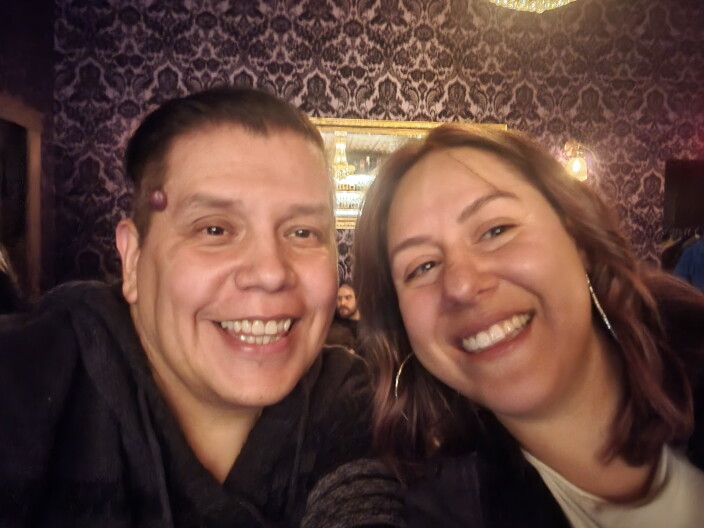 A man and a woman taking a selife style photo from the shoulders up. They both are smiling with teeth showing.