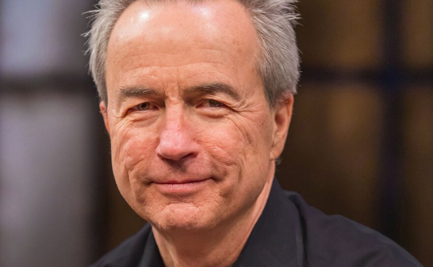 A man with short grey hair wears a black button-down shirt.