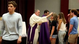 Deacon Steve Brown administers ashes to students during a campus observance of Ash Wednesday, as others wait in line nearby.