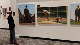 Reds Hall of Fame Director Rick Walls reads the caption on one of the paintings on display.