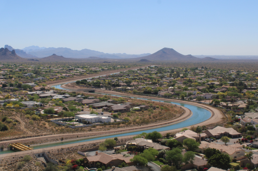 A canal winds through a flat, mostly dry landscape with lots of houses.
