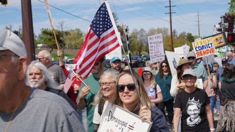 A large crowd of protesters stands along a busy street in Medford, Oregon, holding handmade signs and American flags during a “No Kings” demonstration.