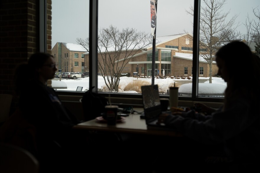 Students sillhouetted in the foreground eat lunch at cafeteria with other school building in the background.