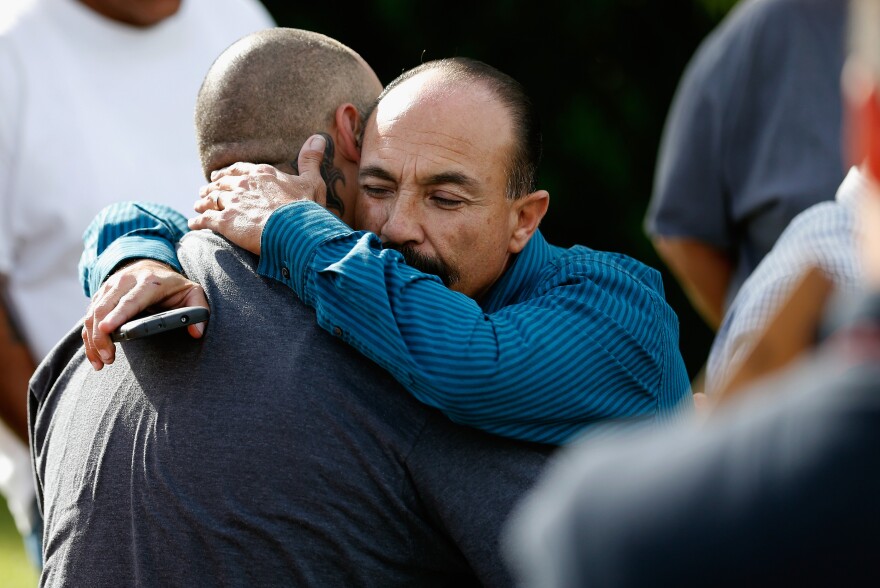 Jesus Gonzalez (left) and Pastor Ernie Ceballos (right) hug outside the crime scene where the suspects of the Inland Resource Center were killed on Wednesday in San Bernardino, Calif.