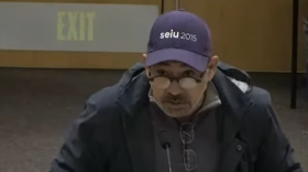 A man in a purple union cap speaks into a microphone.