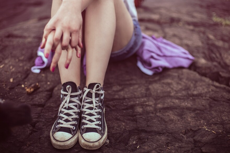 A teen girl sits on the ground, holding her hands together.