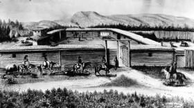 A black and white image of Fort Bridger with men riding horses in front of its walls