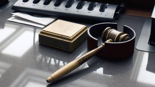 A wooden gavel rests beside a wooden block on a grey desk.