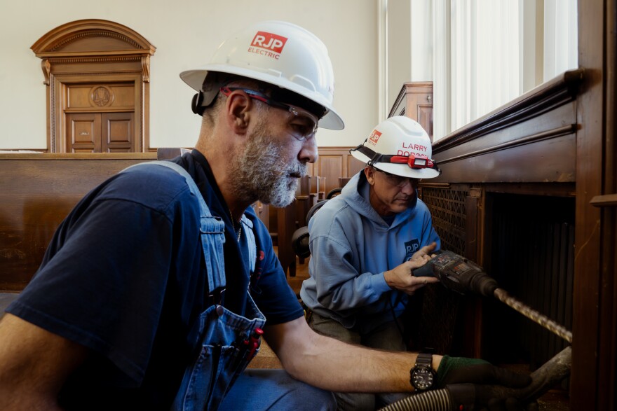RJP Electric’s Rich Mercurio, left, holds a vacuum while Larry Dodson drills large holes in the historic courtroom walls to install upgraded cables for TVs, internet, and speakers on Tuesday, Dec. 9, 2025, in downtown St. Louis.