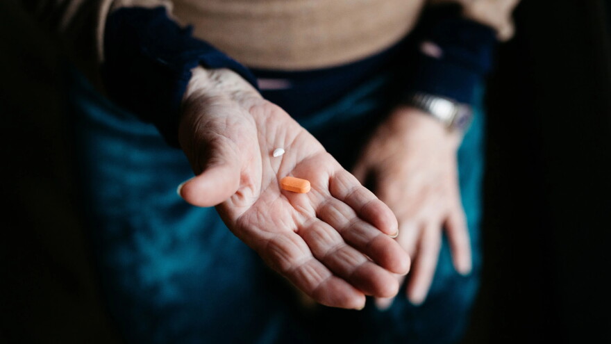 a person holds two pills, one orange and one while, in hands