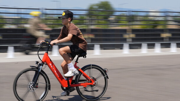A boy in a baseball cap riding a bright red Bikabahn e-bike on a paved path.