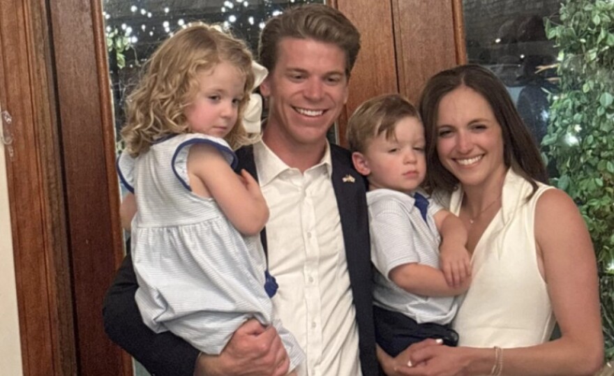 Austin Rogers poses with his wife and two kids, a boy and a girl, in front of a door.