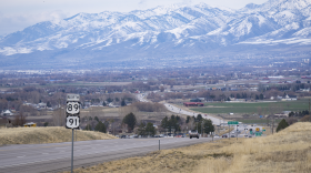 A road leading toward a valley with snowy mountains in the background.