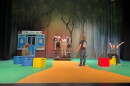 People standing on a green and yellow stage with red, blue and yellow blocks around the floor.