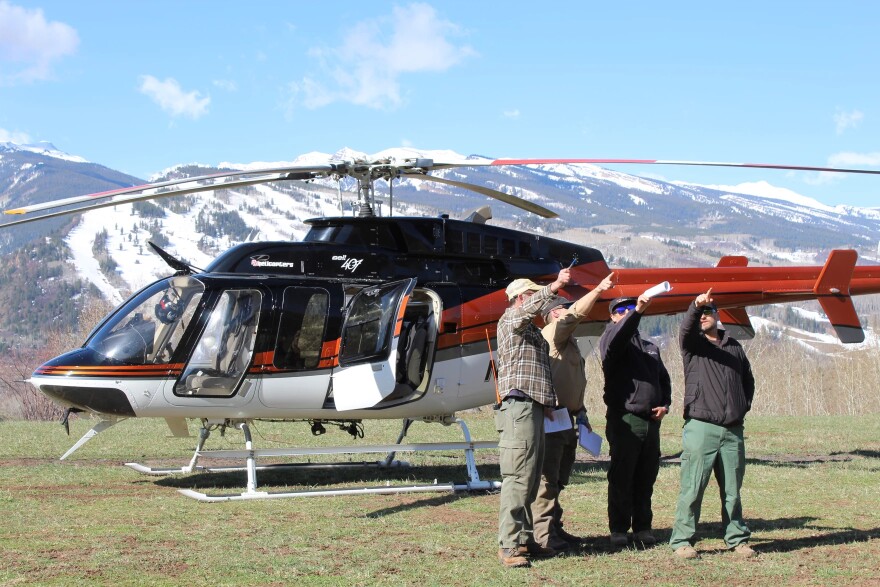 Four men point off into the distance while standing in front of a helicopter