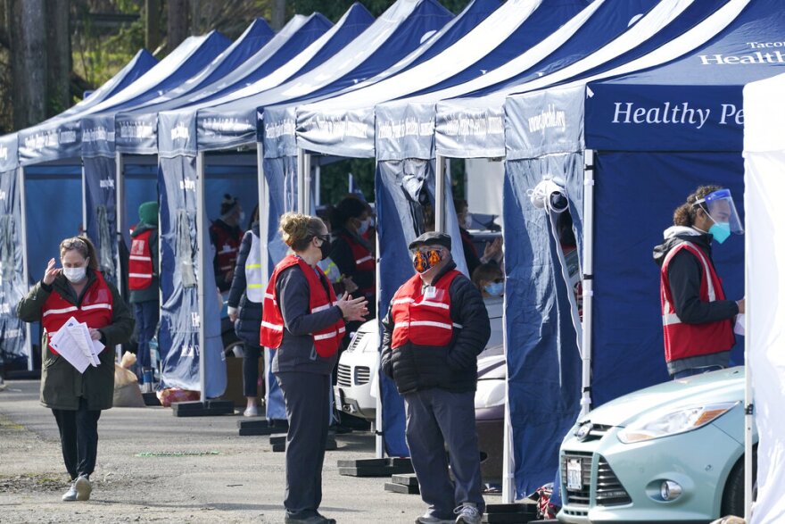 Workers stand near tents at a drive-up mass vaccination site Thursday, March 4, 2021, in Puyallup.