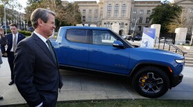 Gov. Brian Kemp smiles as he stands next to a Rivian electric truck during a ceremony to announce that the electric truck maker plans to build a $5 billion battery and assembly plant east of Atlanta projected to employ 7,500 workers, on Thursday, Dec. 16, 2021, in Atlanta.