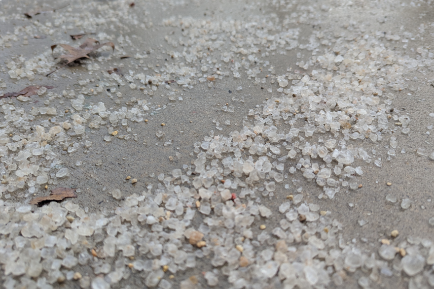 Some of the salt is slightly brown, while the rest is white or clear. There are a few leaves on the sidewalk.
