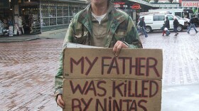 Panhandler holds sign in front of Pike Place Market. Sign reads "My father was killed by ninjas. Need money for karate lessons."
