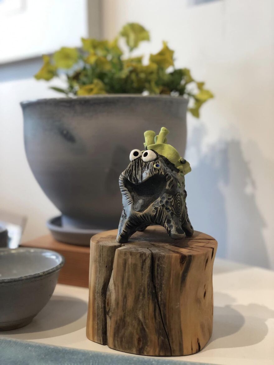  A ceramic fungal character on a stand of wood in front of a potted plant