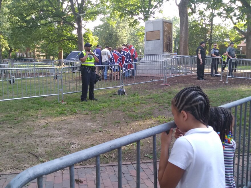 New Confederate States of America members pray at the fallen Silent Sam statue as protesters continue to chant against them on Saturday, Sept. 8, 2018. 