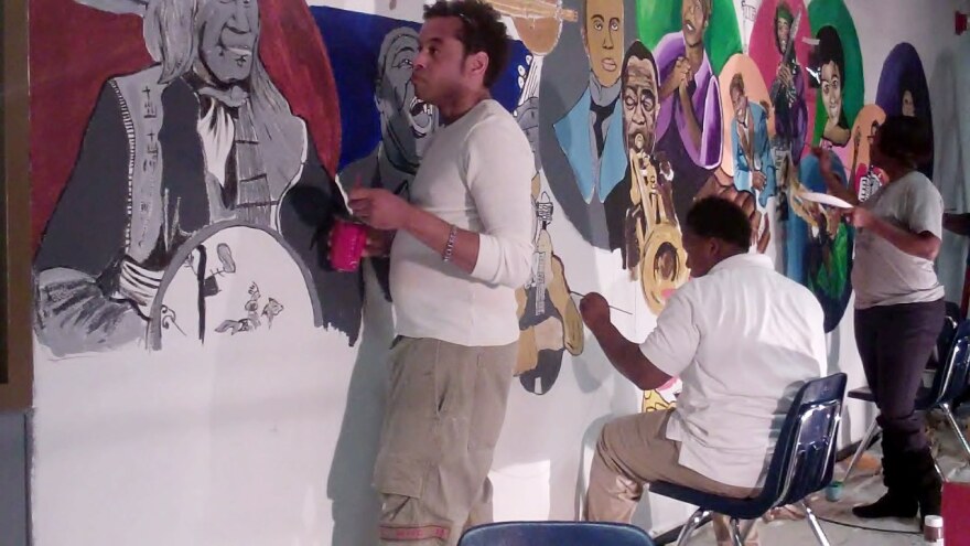 Artist Jamar Pierre (leftt) and students at West St. John High School work on a mural project.