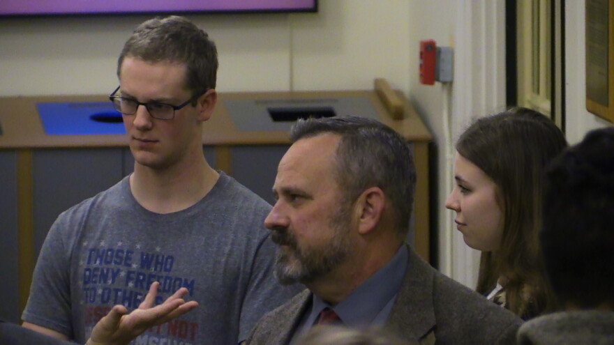 Two students and an audience member listen to a candidate speak in the lobby of a university building.