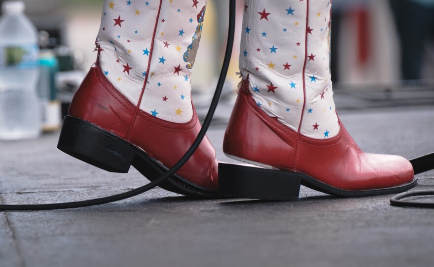 Cowboy boots with a red base with a white and star-spangled design. Stars are red, blue and yellow. One of the heels is detached from the shoe.