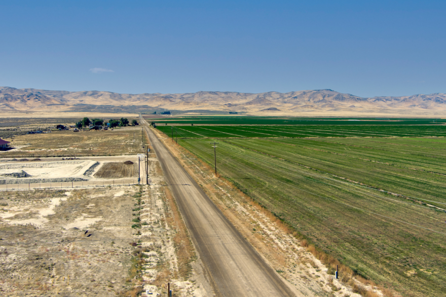 Agricultural fields in a mountain valley with a road running through them. One side is mostly green while the other is more barren.