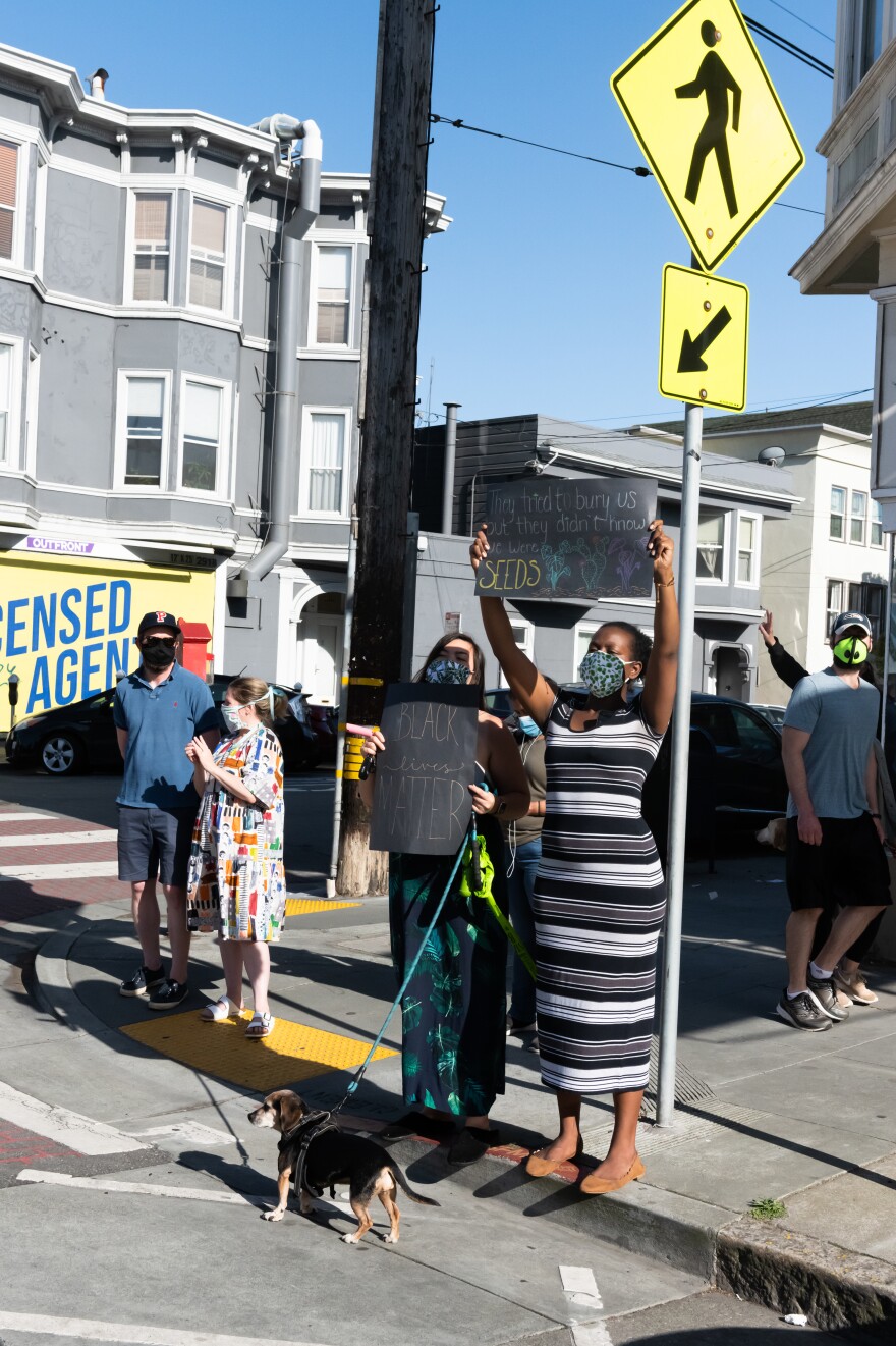 A protester holds a sign up in San Francisco as a caravan of cars drives by, in a socially distanced demonstration denouncing police brutality against black Americans. Bikers, pedestrians and residents along the caravan route participated in the protest.