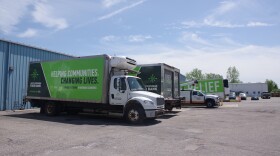 Several trucks with green ang grey designs on them are parked at a loading dock. The truck closest to the camera reads "South Michigan Food Bank, Helping Communities. Changing Lives"