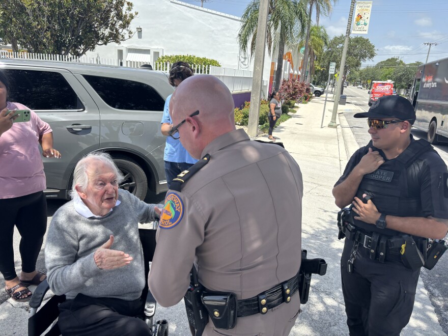 Florida Highway Patrol troopers, including a captain, talk to community advocate and priest, Father Frank O'Loughlin. He has spent decades advocating for the Guatemalan diaspora in Palm Beach County and tried to negotiate a peace between officers and the man locked inside the bakery during the tense immigration operation on July 9, 2026.
