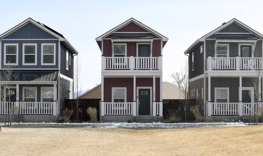 Three matching homes sit side by side. Each is two stories and sit in dirt fields.