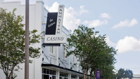 White building with black and white sign reading the historic Manhattan Casino with trees around it 