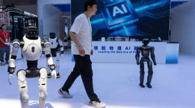 A worker passes by robots from Chinese company Lens at the China International Supply Chain Expo in Beijing on Monday, June 22, 2026. (Ng Han Guan/AP)