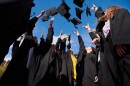 Low angle view of six young graduates in black gowns, throwing their mortarboards in the air 