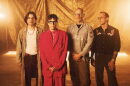 Group of four men stands together with glowing light behind them 