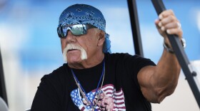 Hulk Hogan is seen with a blue bandana, black T-shirt and sunglasses, sitting in a golf cart
